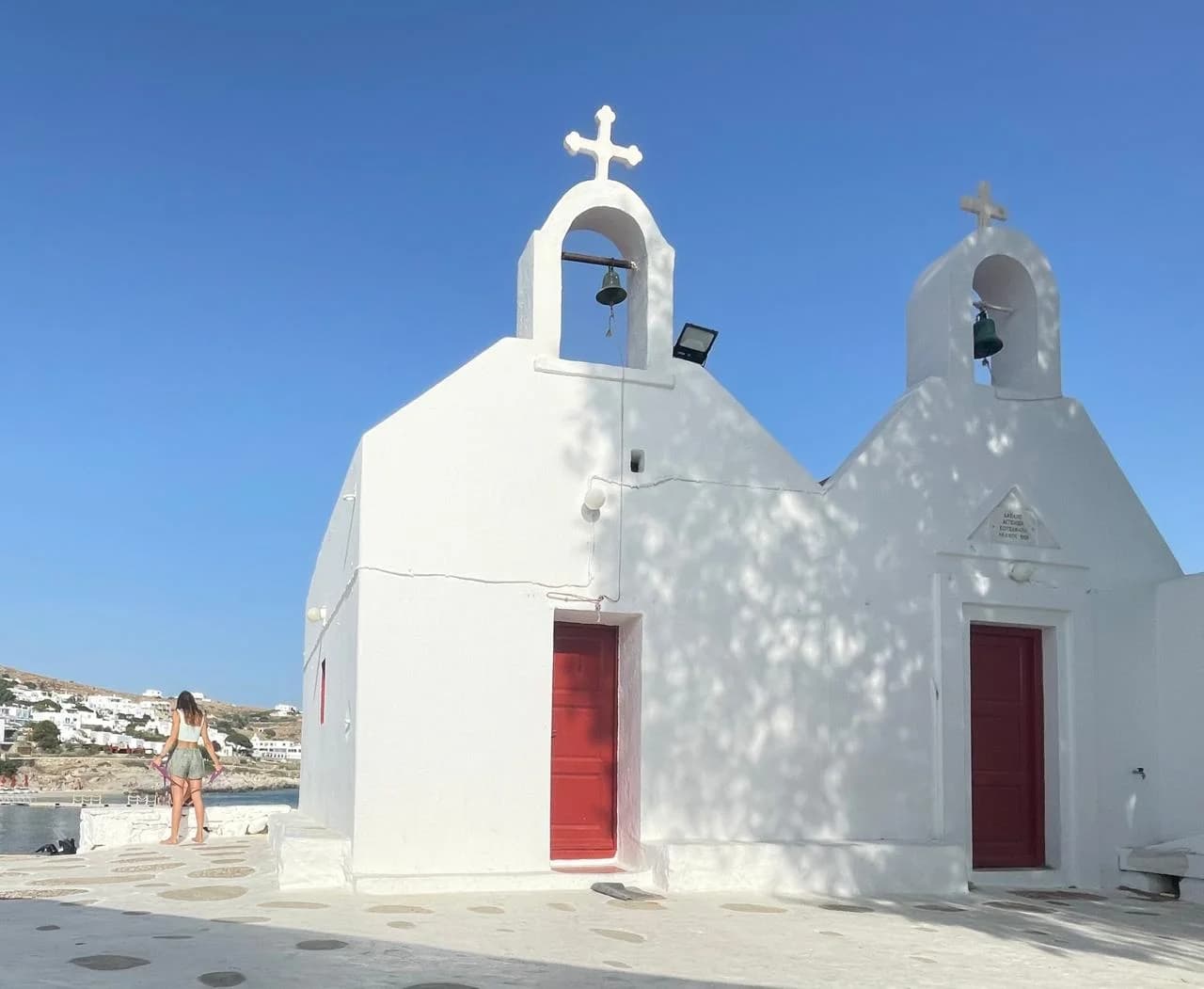 Whitewashed Mykonos chapel with red doors beside the sea